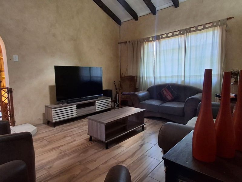 A living room featuring exposed timber ceiling beams, tiled flooring, and an arched entryway leading to adjacent spaces.