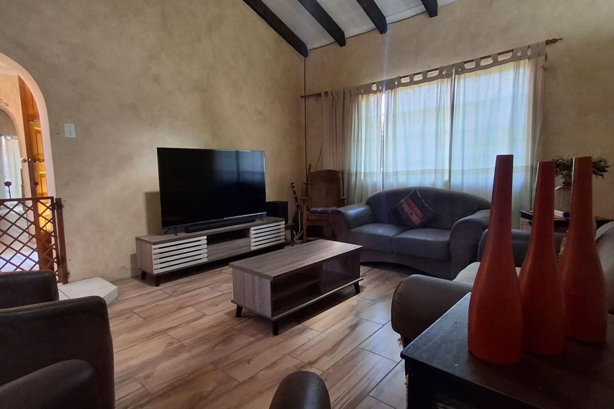 A living room featuring exposed timber ceiling beams, tiled flooring, and an arched entryway leading to adjacent spaces.