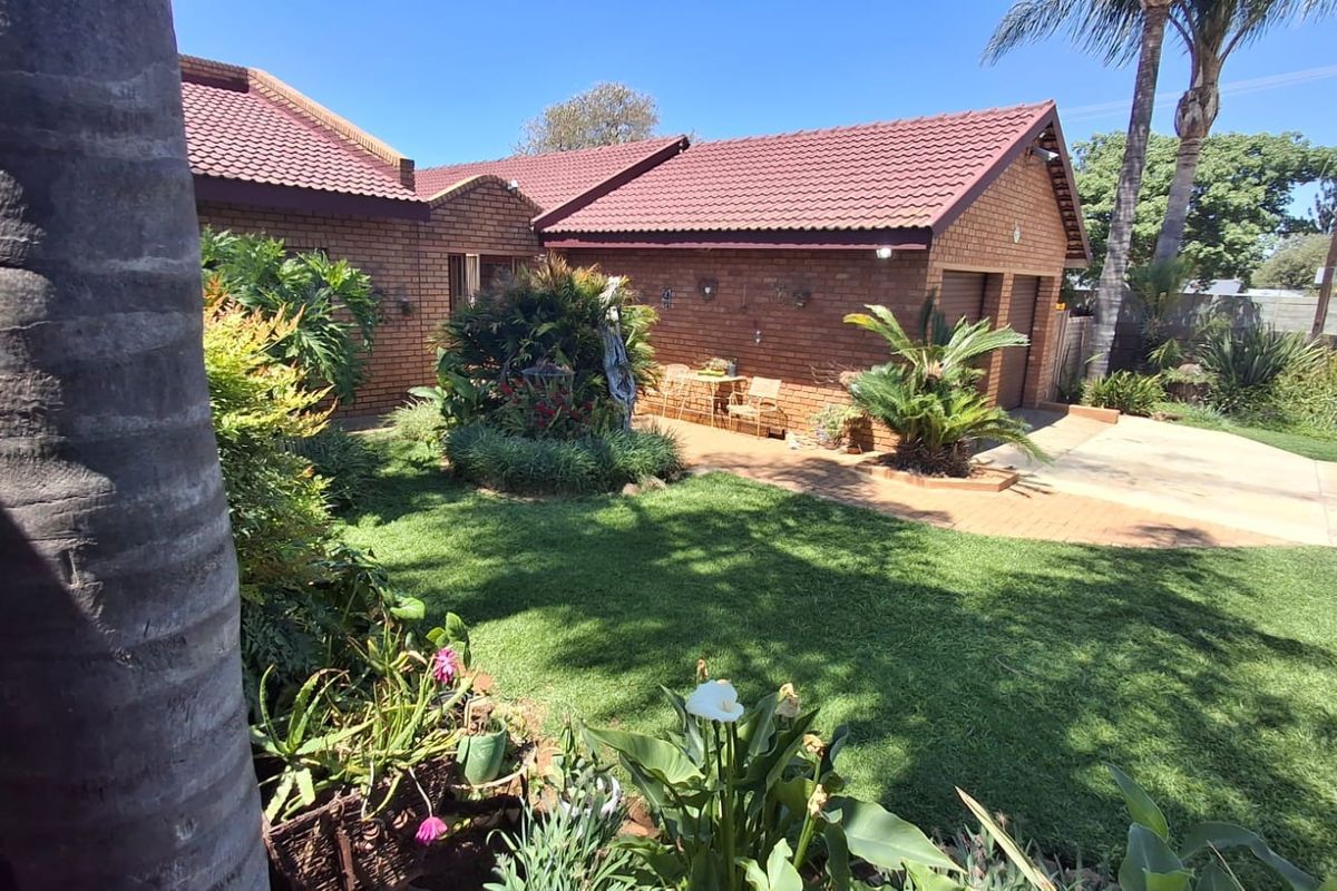 A well-maintained rear garden featuring a brick facade, tiled roof, and a double garage with a paved driveway.