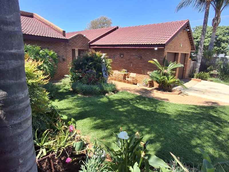 A well-maintained rear garden featuring a brick facade, tiled roof, and a double garage with a paved driveway.