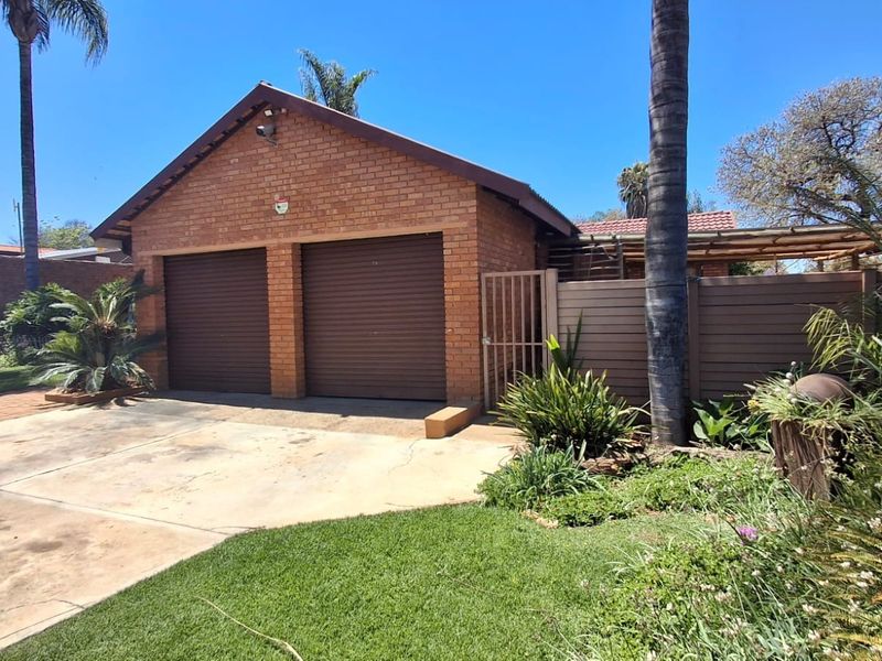 A detached double garage featuring a brick exterior, roller doors, and a concrete driveway, set within a landscaped garden area.