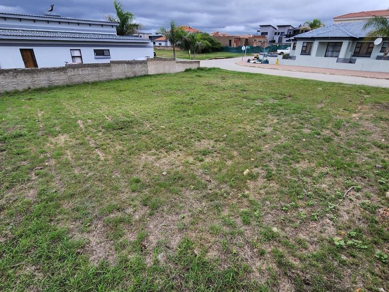 A vacant residential plot featuring a grass lawn and boundary wall, situated in a developed neighborhood.