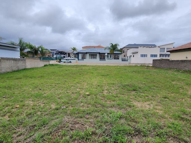 A vacant residential plot featuring a grass lawn and perimeter boundary walls, situated in a developed neighborhood.