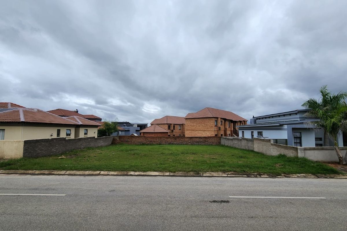 A vacant residential plot situated between existing homes, featuring a level grass surface and established boundary walls in a developed neighborhood.