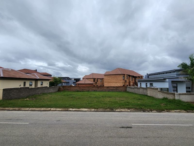 A vacant residential plot situated between existing homes, featuring a level grass surface and established boundary walls in a developed neighborhood.