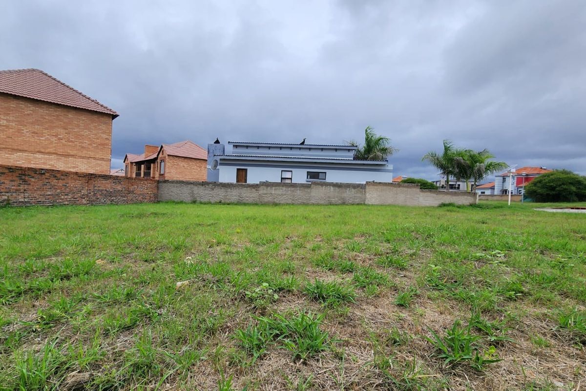 A view of a vacant residential plot featuring a grass lawn and perimeter brick walling, situated in a developed neighborhood.