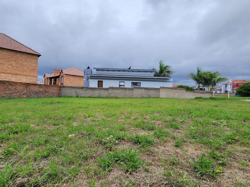 A view of a vacant residential plot featuring a grass lawn and perimeter brick walling, situated in a developed neighborhood.