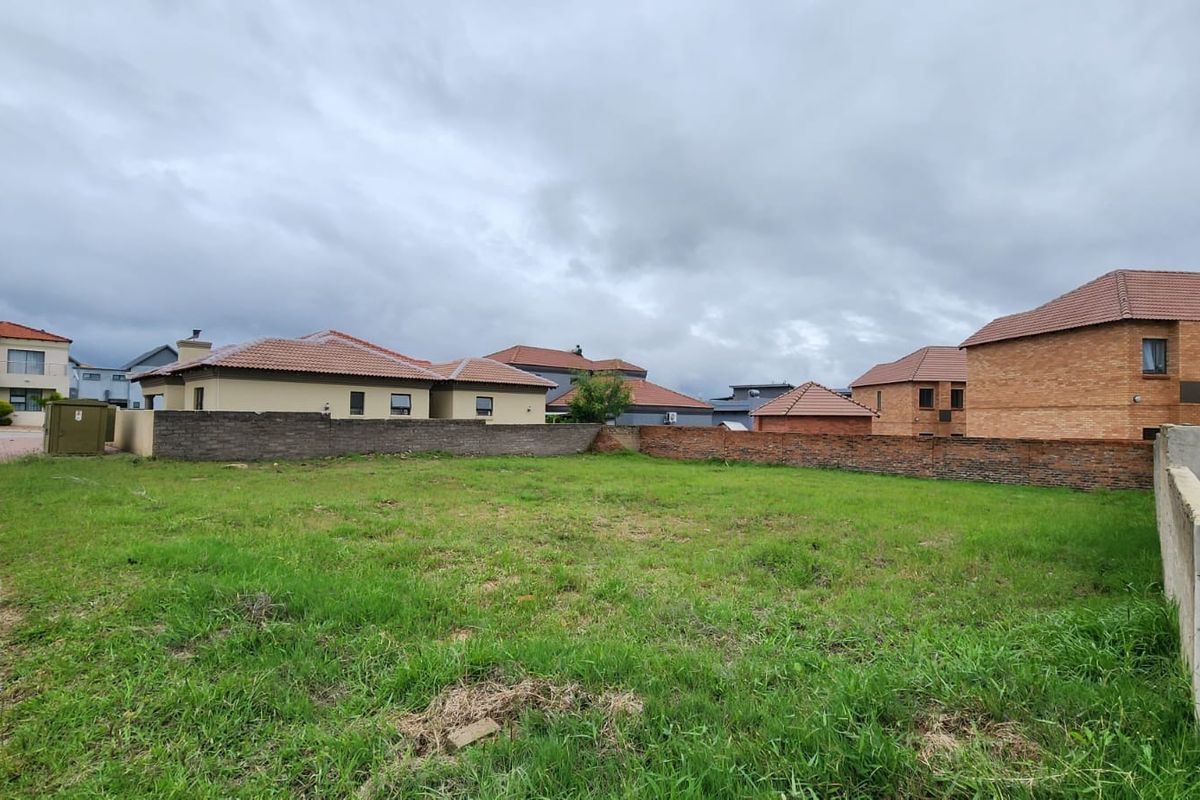 A vacant residential plot featuring a grass lawn and perimeter boundary walls, situated within an established suburban neighborhood.