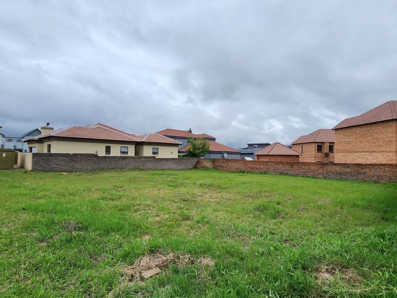 A vacant residential plot featuring a grass lawn and perimeter boundary walls, situated within an established suburban neighborhood.