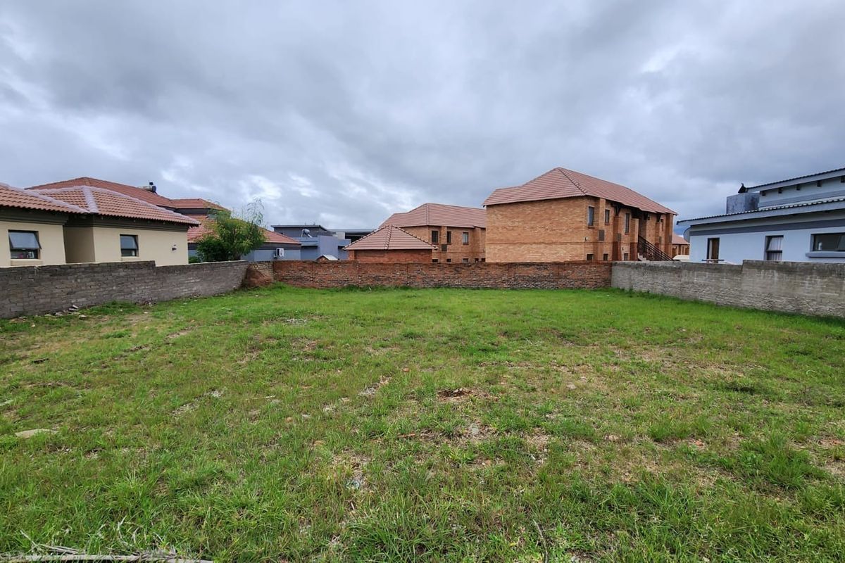 A vacant residential plot featuring a grass lawn enclosed by perimeter brick walls, situated within a developed neighborhood.