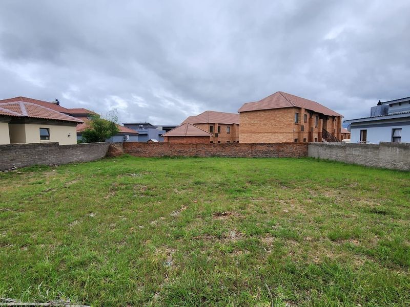 A vacant residential plot featuring a grass lawn enclosed by perimeter brick walls, situated within a developed neighborhood.