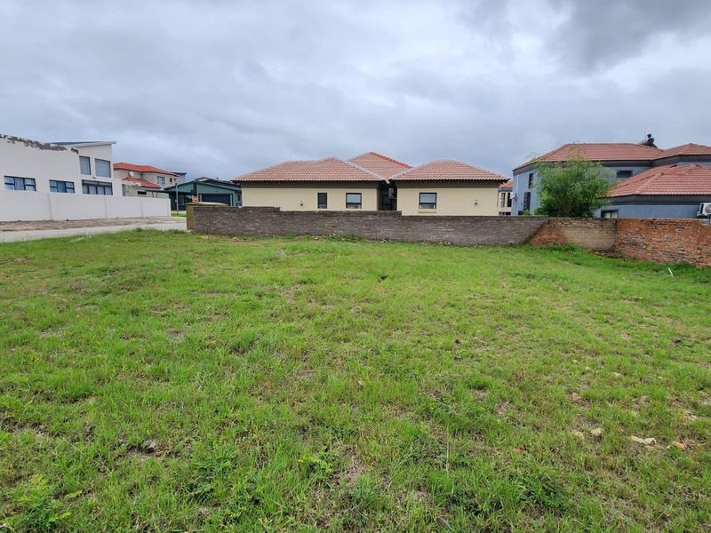 A vacant residential plot featuring a grass lawn and perimeter boundary walls, situated in a developed residential neighborhood.