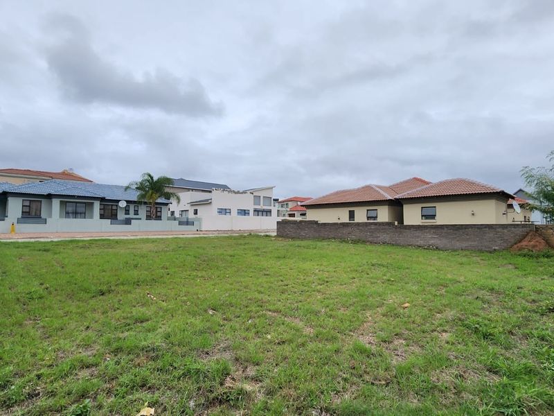 A vacant residential plot of land featuring a grass lawn and boundary wall, situated in a developed neighborhood.