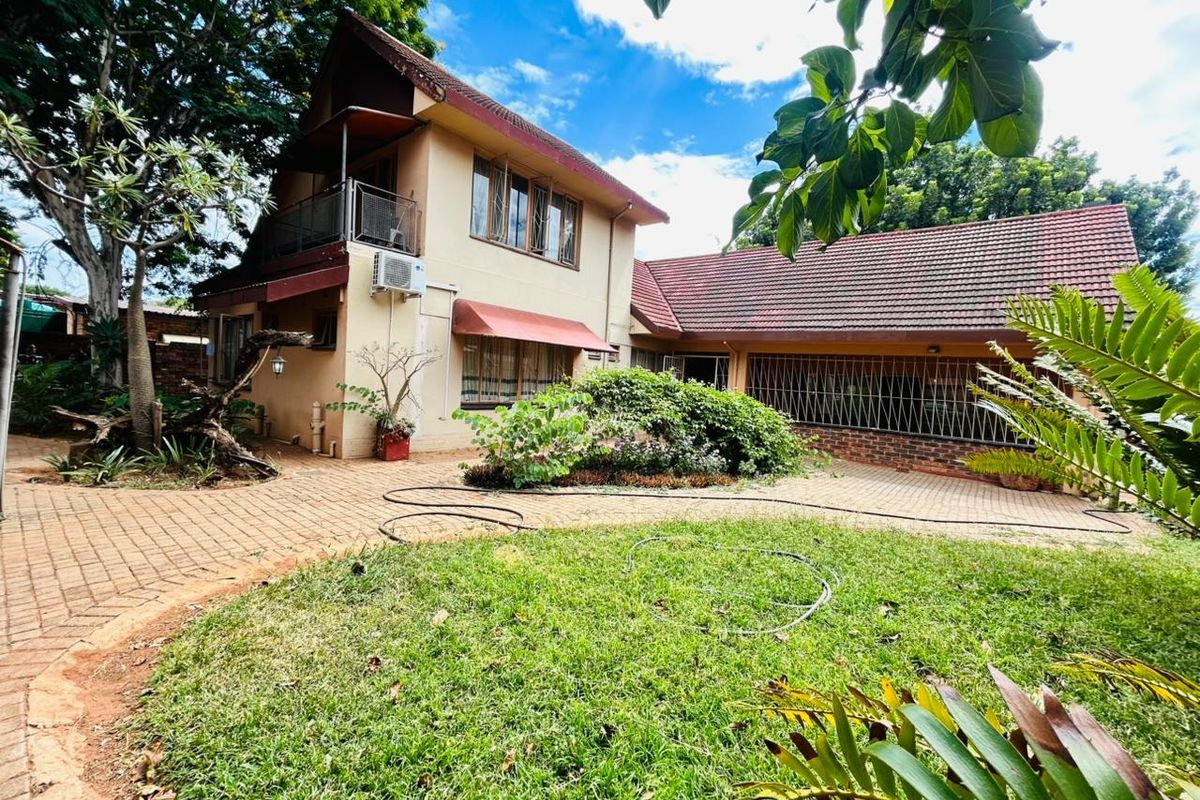 Rear view of a two-story house featuring a tiled roof, balcony, paved courtyard, and established garden area.