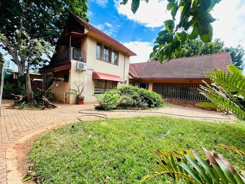 Rear view of a two-story house featuring a tiled roof, balcony, paved courtyard, and established garden area.
