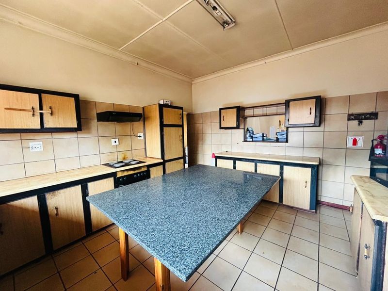A dated kitchen featuring built-in cabinetry, a central stone-topped island, tiled flooring, and a tiled backsplash with an integrated stove and extractor fan.