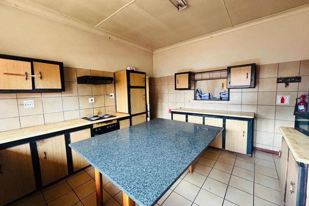A dated kitchen featuring built-in cabinetry, a central stone-topped island, tiled flooring, and a tiled backsplash with an integrated stove and extractor fan.