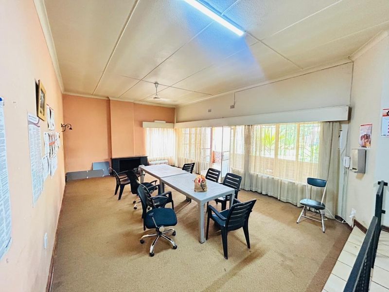 Spacious living area featuring a built-in fireplace, large windows with security bars, and fluorescent lighting, offering a versatile space for renovation.