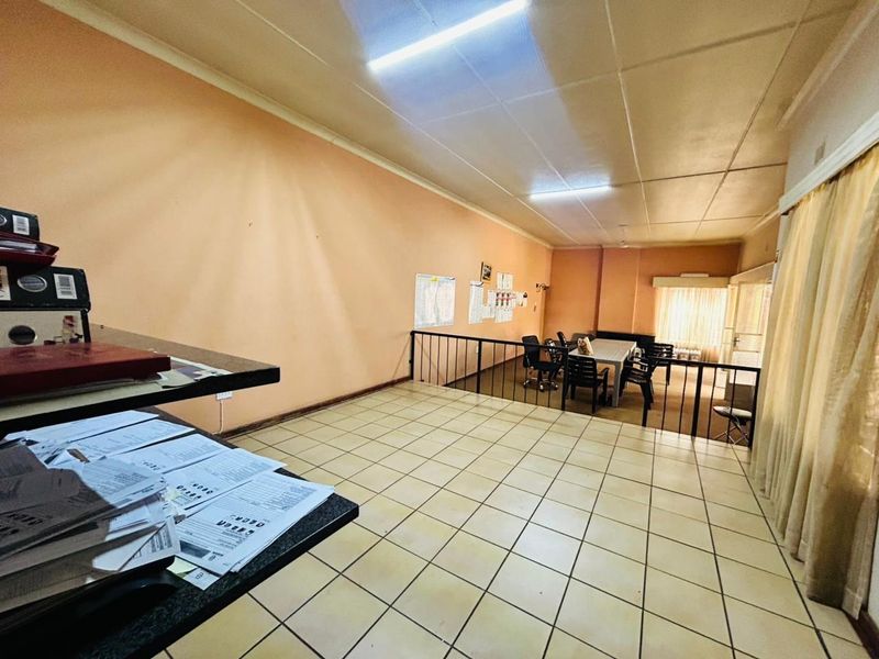 A spacious living area featuring tiled flooring, a metal balustrade, and fluorescent lighting, offering a functional layout with potential for modernization.