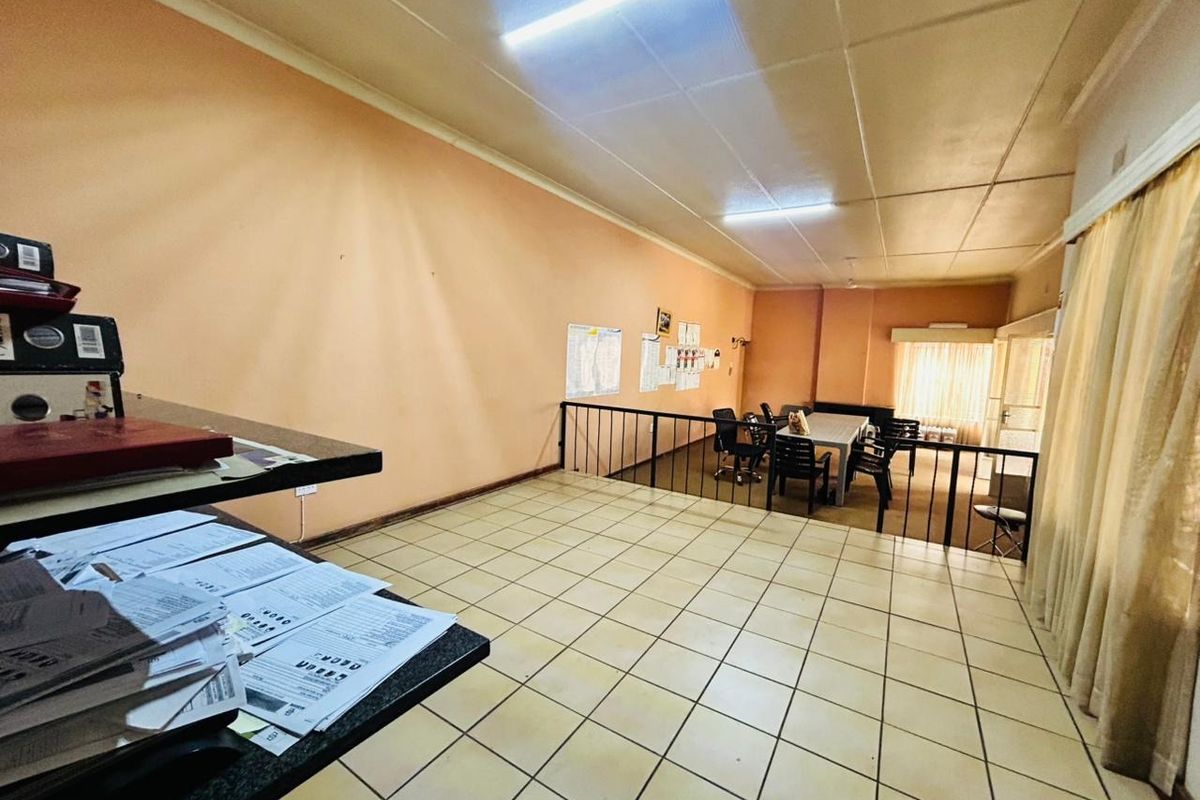 A spacious living area featuring tiled flooring, a metal balustrade, and fluorescent lighting, offering a functional layout with potential for modernization.