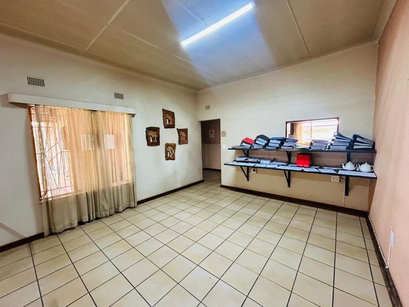 A functional office space featuring ceramic floor tiles, wall-mounted shelving, and security bars on the window, suitable for a home workspace.