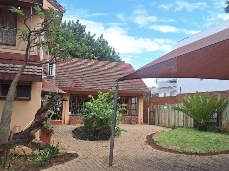 Rear exterior view featuring a paved courtyard, shade sail, and established garden area with brick boundary walling.