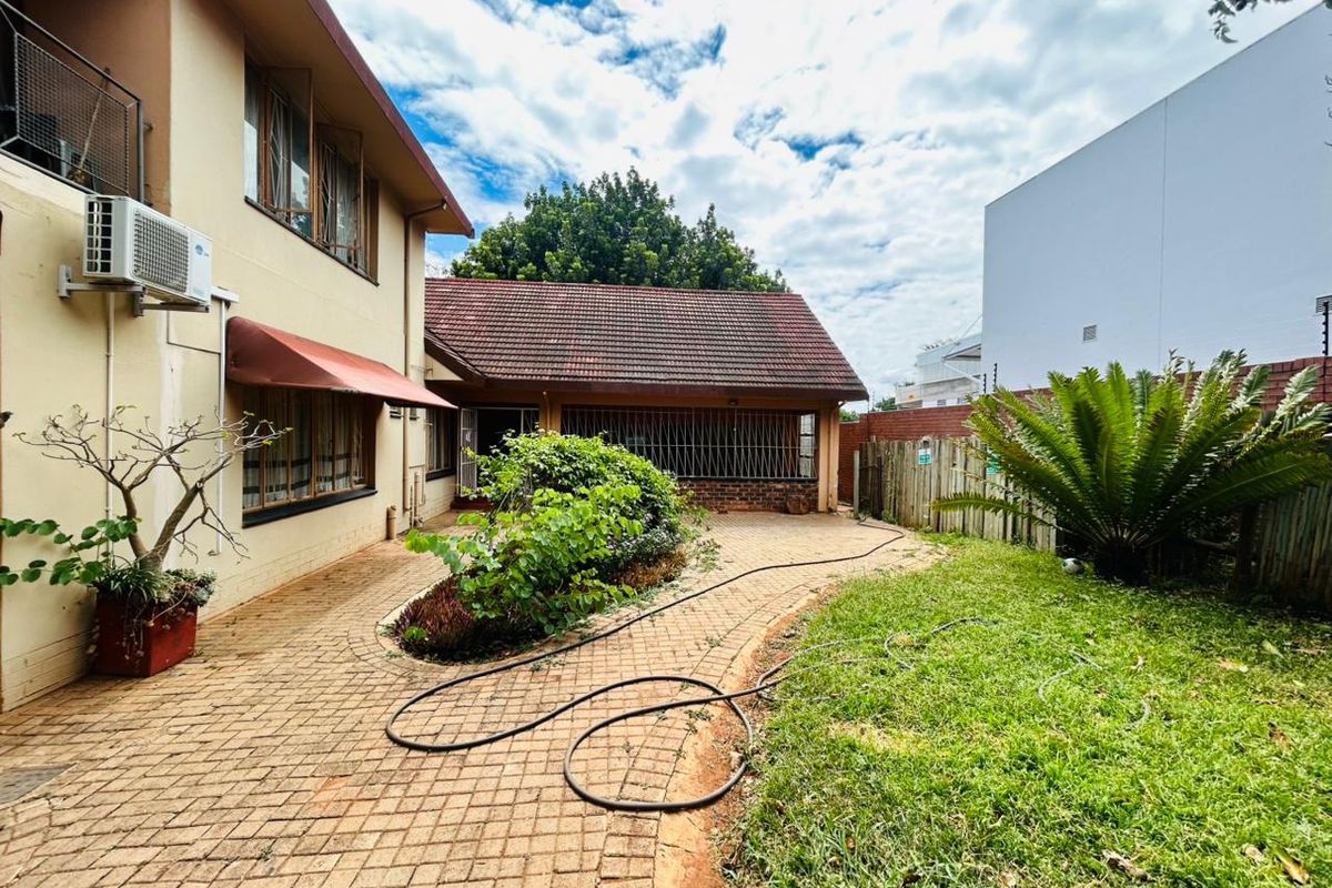 Rear exterior view of the property featuring a paved courtyard, landscaped garden area, and tiled roof structure.