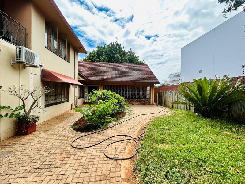 Rear exterior view of the property featuring a paved courtyard, landscaped garden area, and tiled roof structure.