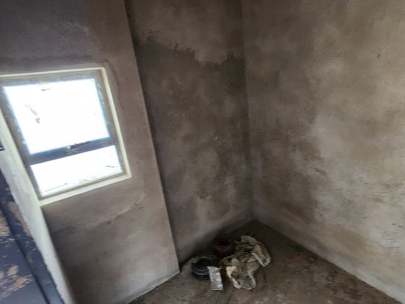 An unfinished utility space featuring raw plaster walls and a window, currently in a shell condition awaiting final finishes.