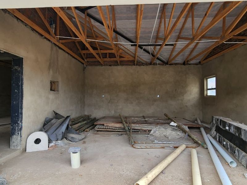 An unfinished utility space or garage area featuring exposed timber roof trusses, raw plastered walls, and a concrete floor, currently used for storage.