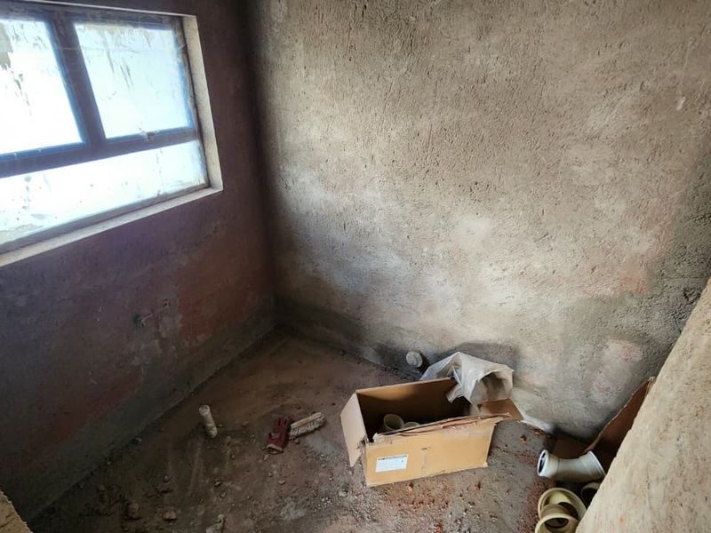 An unfinished utility space or small room featuring raw plaster walls, concrete flooring, and a window, currently in a shell state requiring completion.
