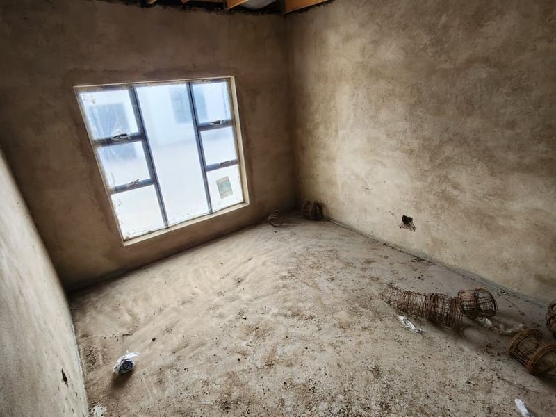 An unfinished bedroom space featuring raw plastered walls, an aluminium window frame, and exposed concrete flooring, awaiting final finishes and interior detailing.