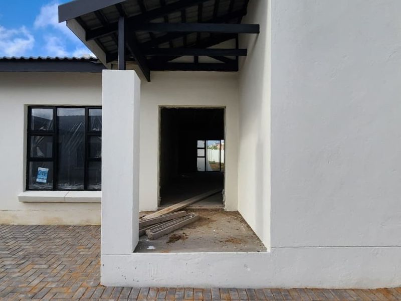 Front exterior view of a townhouse under construction, featuring a paved driveway, covered entrance, and modern aluminum window frames.