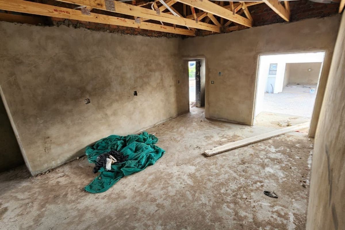 An unfinished interior space in the construction phase, featuring exposed timber roof trusses, raw cement plastered walls, and concrete flooring.