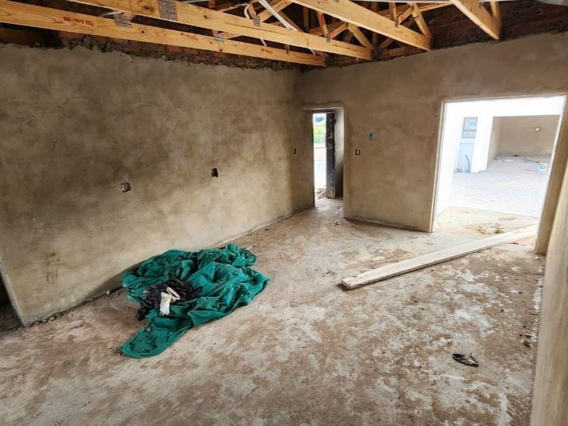 An unfinished interior space in the construction phase, featuring exposed timber roof trusses, raw cement plastered walls, and concrete flooring.