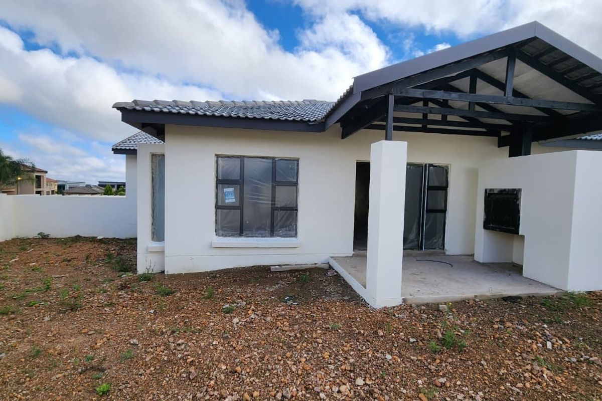 Rear view of the townhouse featuring a covered patio with a built-in braai, aluminium window frames, and an unlandscaped garden area.