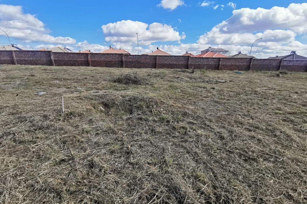 A vacant residential plot featuring dry grass and a secure perimeter brick wall, offering a blank canvas for future development.