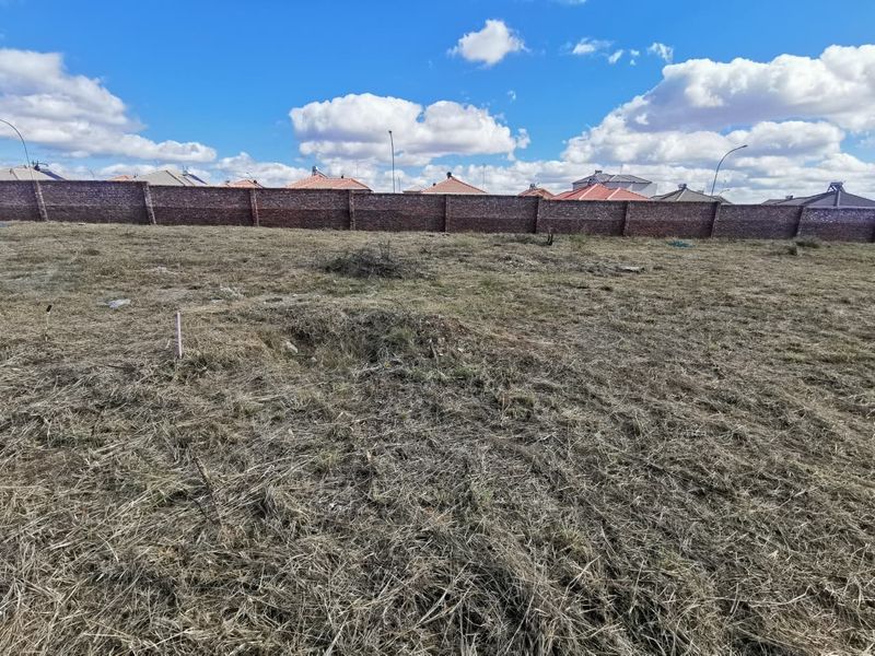 A vacant residential plot featuring dry grass and a secure perimeter brick wall, offering a blank canvas for future development.