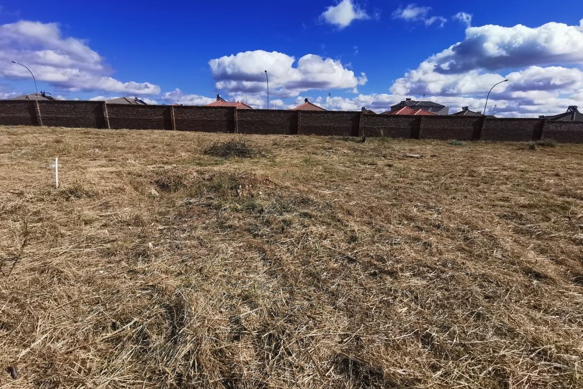 A vacant residential plot featuring dry grass and a secure perimeter brick wall, offering a clear space for future development.