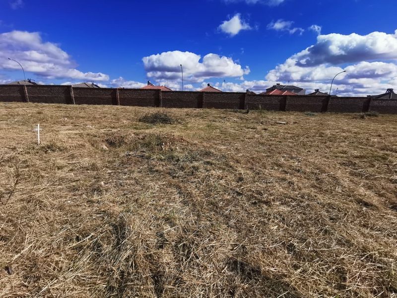 A vacant residential plot featuring dry grass and a secure perimeter brick wall, offering a clear space for future development.