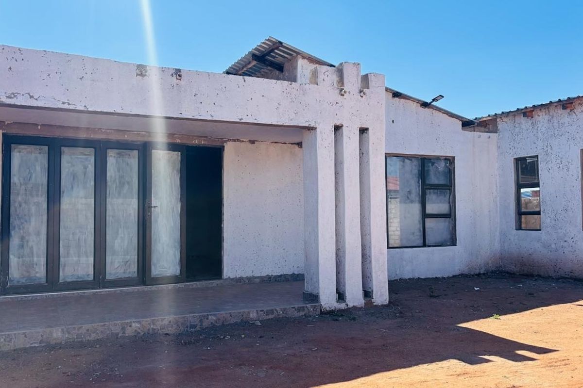 Rear exterior view of the property featuring a covered patio, aluminium sliding doors, and significant wear to the exterior wall finishes and roof structure.
