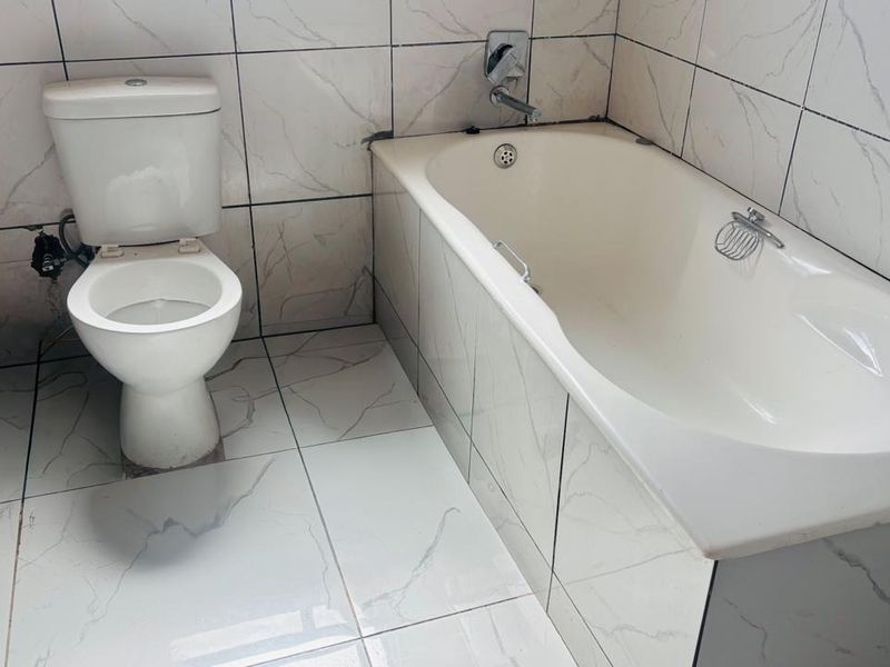 A functional bathroom featuring a standard toilet and a built-in bathtub with tiled walls and flooring throughout.