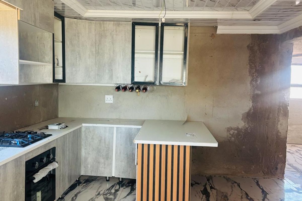 A kitchen in the process of renovation featuring modern cabinetry, a gas hob, built-in oven, and marble-look flooring, requiring final wall finishes.