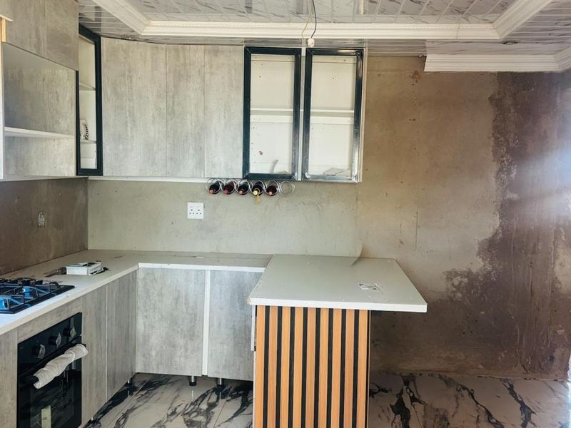 A kitchen in the process of renovation featuring modern cabinetry, a gas hob, built-in oven, and marble-look flooring, requiring final wall finishes.