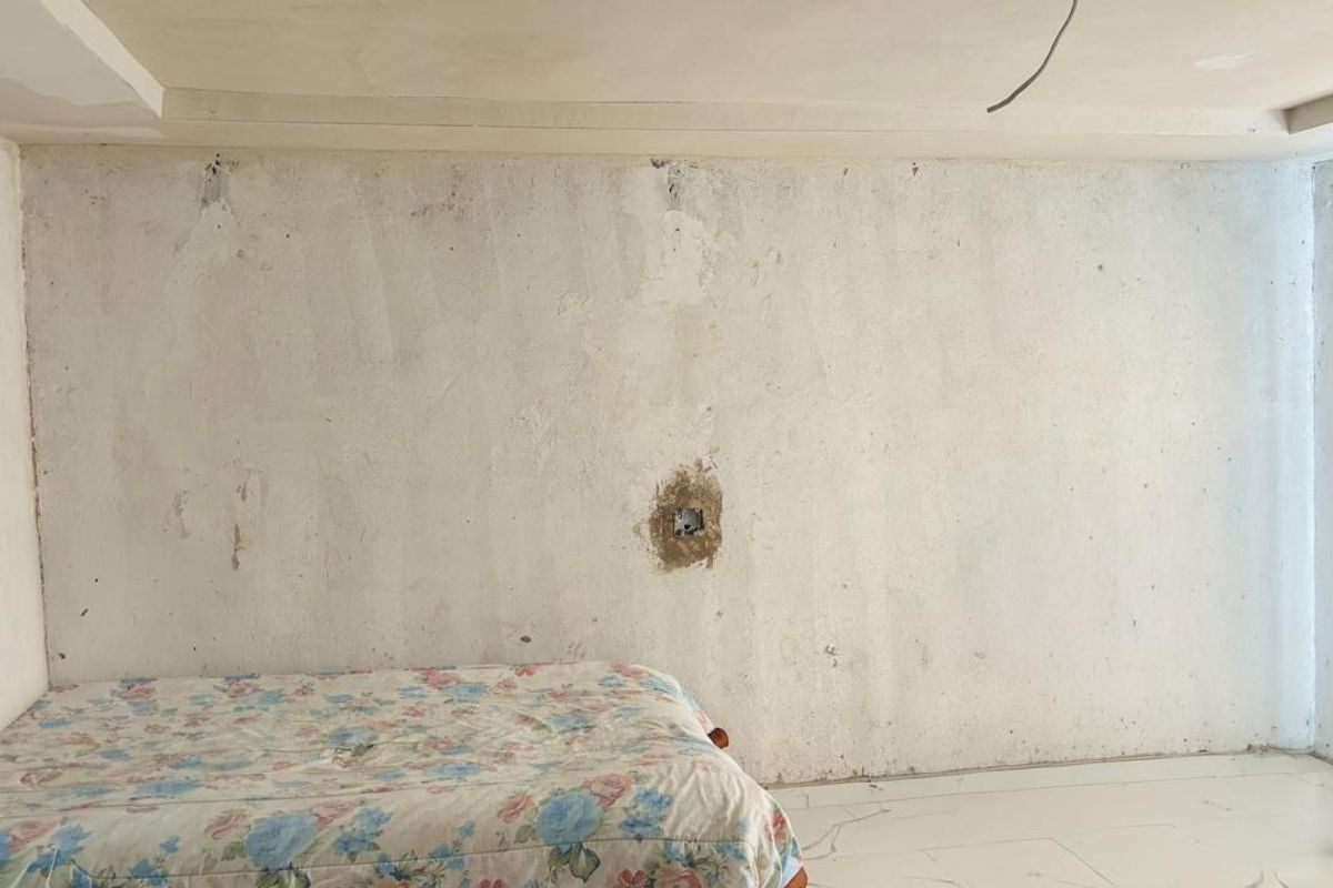 A bedroom in need of renovation, featuring tiled flooring and unfinished wall surfaces with exposed electrical wiring.