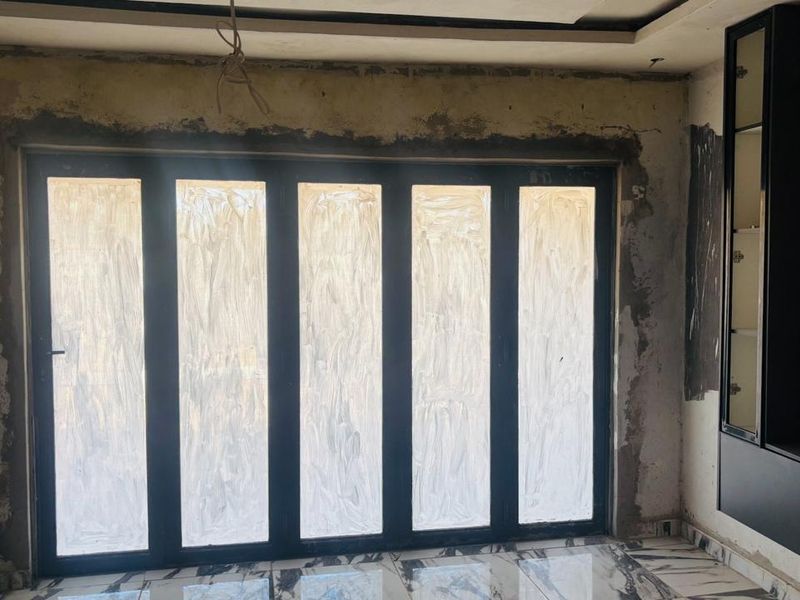 An unfinished living room space featuring large black bi-fold doors, marble-look floor tiles, and built-in cabinetry, currently undergoing renovation.