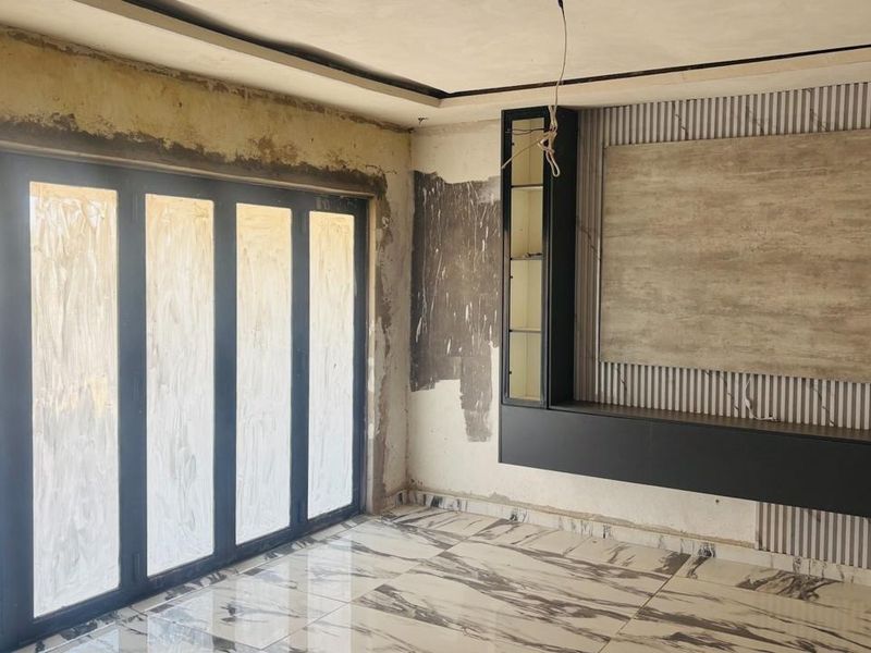 An unfinished living room featuring large bi-fold doors, marble-look tiled flooring, and a custom built-in media unit requiring final wall finishes and electrical completion.