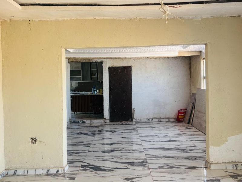 An open-plan living and kitchen area currently under renovation, featuring marble-look floor tiles and requiring finishing work on walls and electrical fixtures.