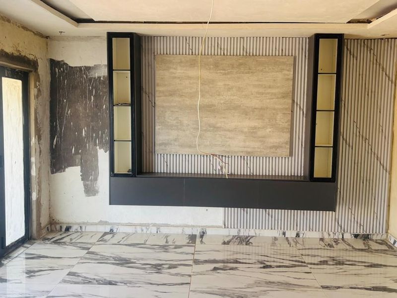 Living room featuring a modern built-in media unit, marble-look floor tiles, and bi-fold doors, currently undergoing renovation with unfinished wall surfaces.