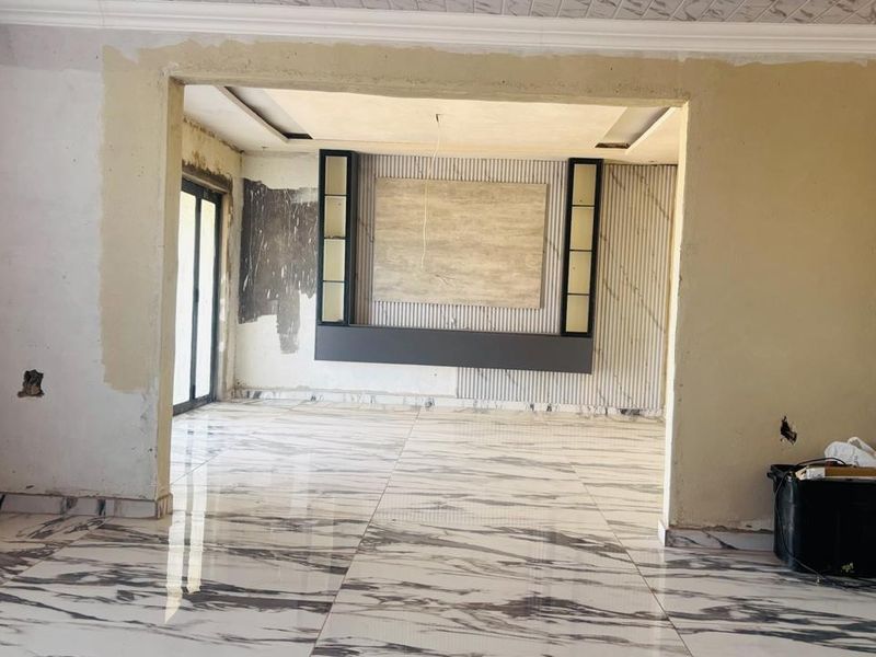 Spacious living area featuring marble-look floor tiles and a custom built-in media wall, currently undergoing renovation with unfinished wall surfaces.